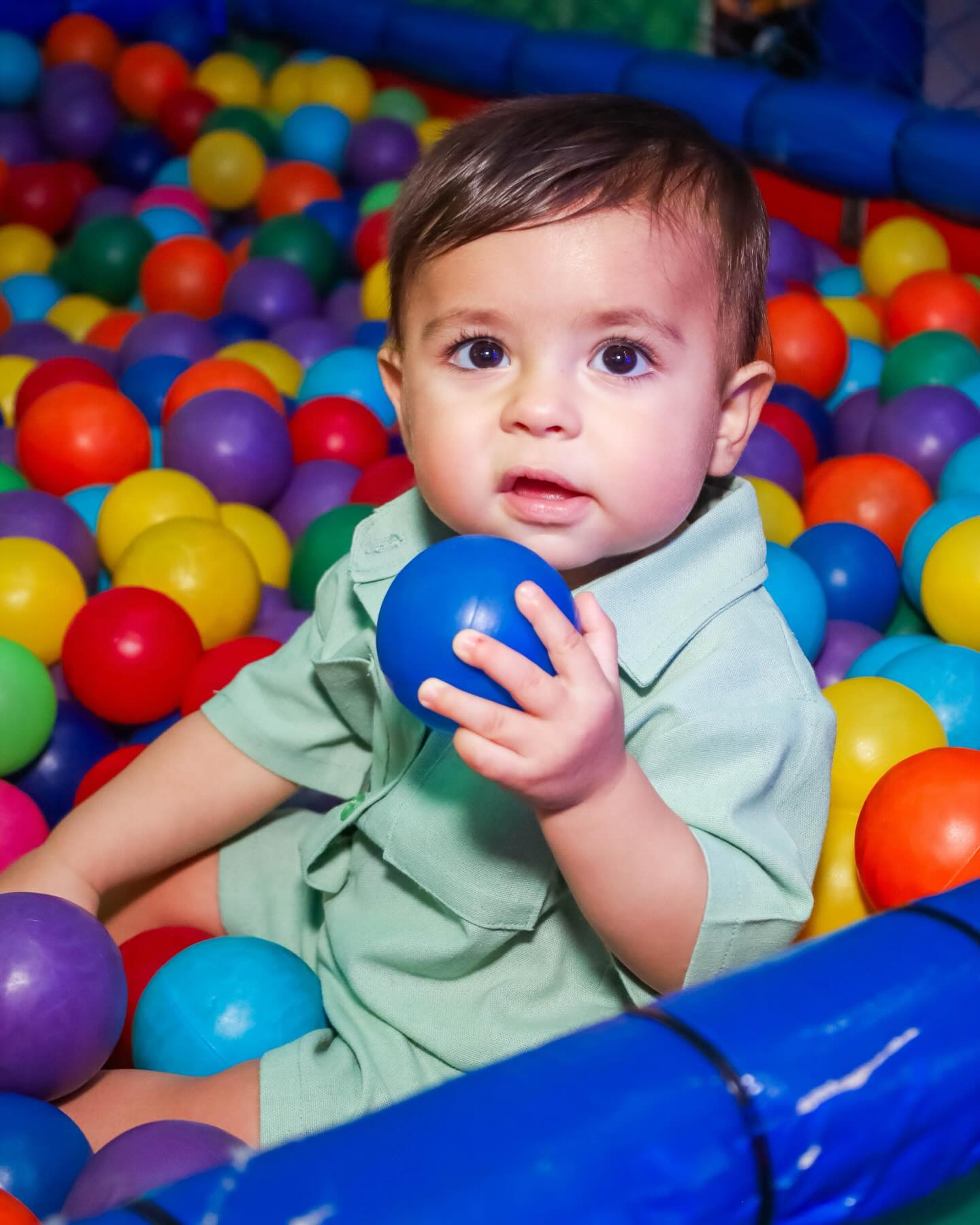 Menino sentado em uma piscina de bolinhas coloridas segurando uma bola azul