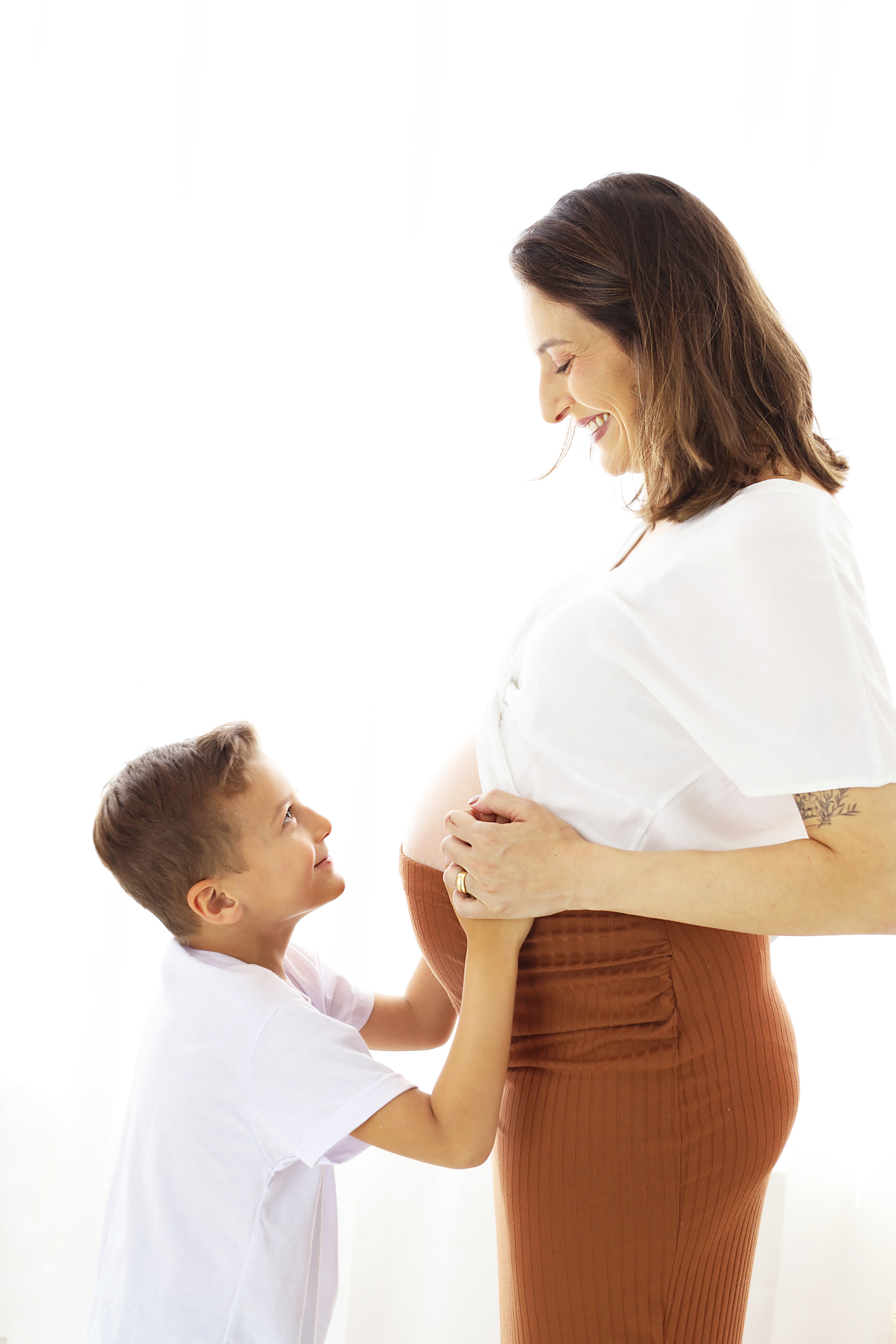 Menino sorrindo para a mãe gestante, com as mãos sobre a barriga dela