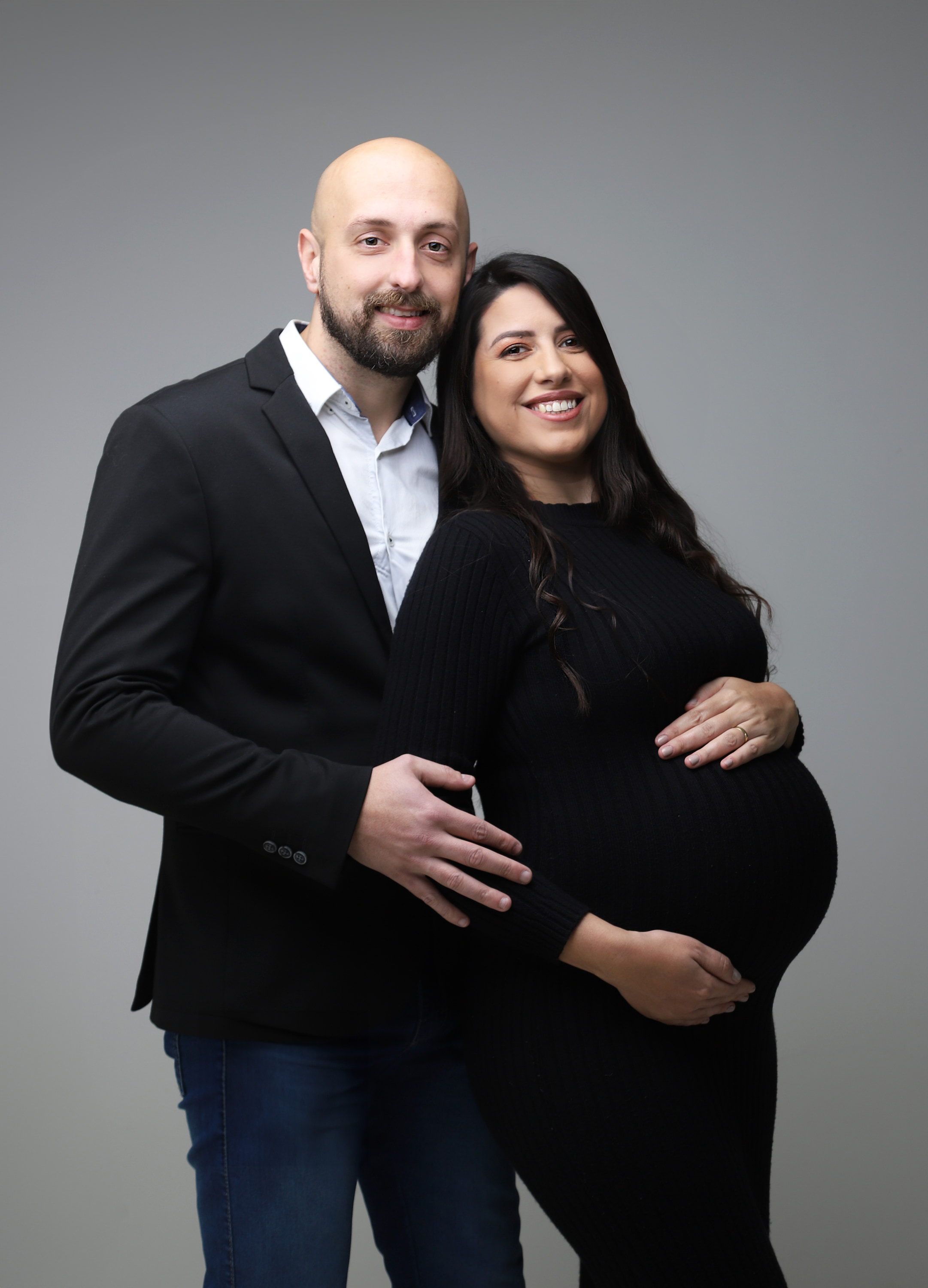 Casal sorrindo em um retrato de gestante, com as mãos sobre a barriga