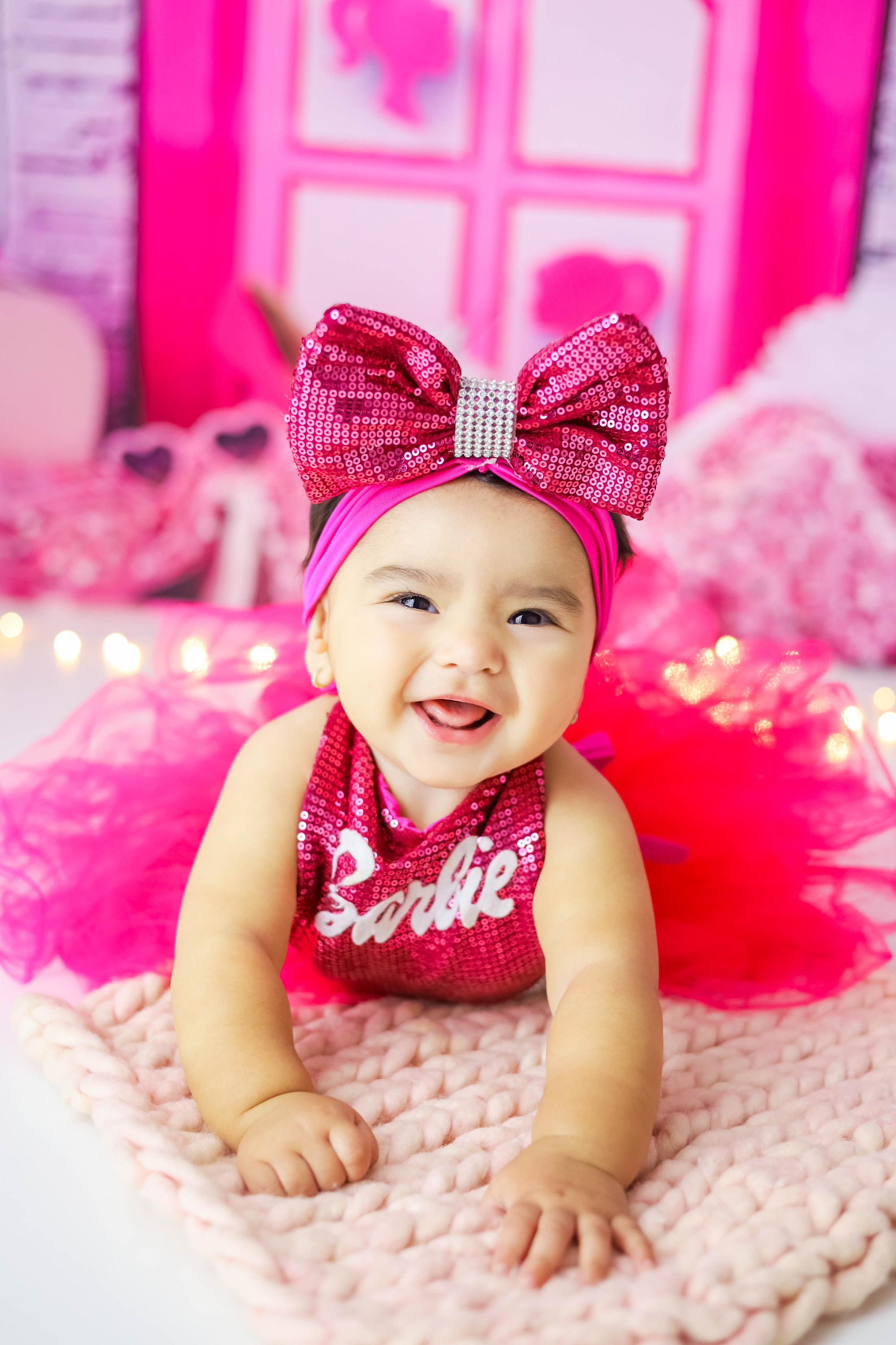 Bebê sorrindo em um cenário rosa, usando um grande laço de lantejoulas
