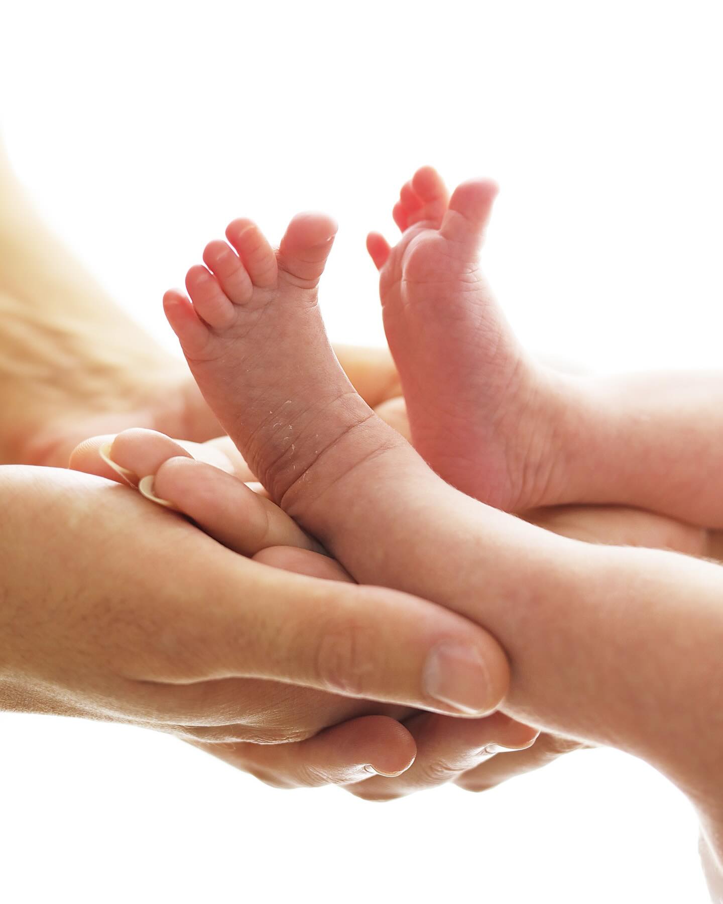 Pezinhos de um recém-nascido acolhidos nas mãos de um adulto
